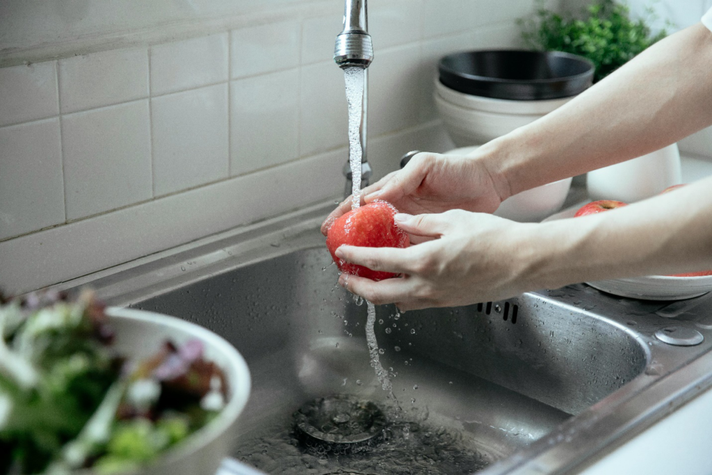 Two hands washing a crisp apple in the kitchen sink after plumbing services cleaned the drain, ensuring cleanliness before consumption.