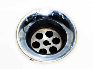 Close-up of a stainless steel sink drain showing signs of corrosion from chemical drain cleaners.